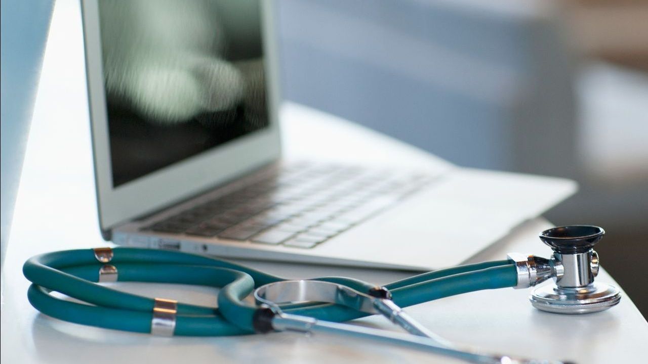 Uno stetoscopio è appoggiato su un tavolo accanto a un computer portatile.