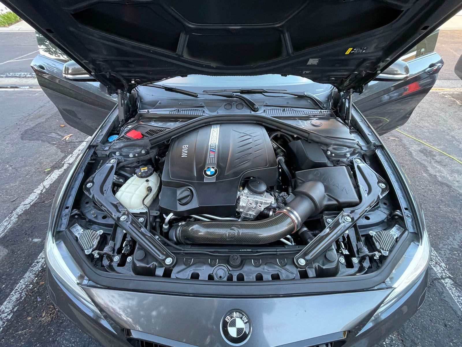 Car engine bay open, showing complex machinery and fluids. Blue car exterior visible.