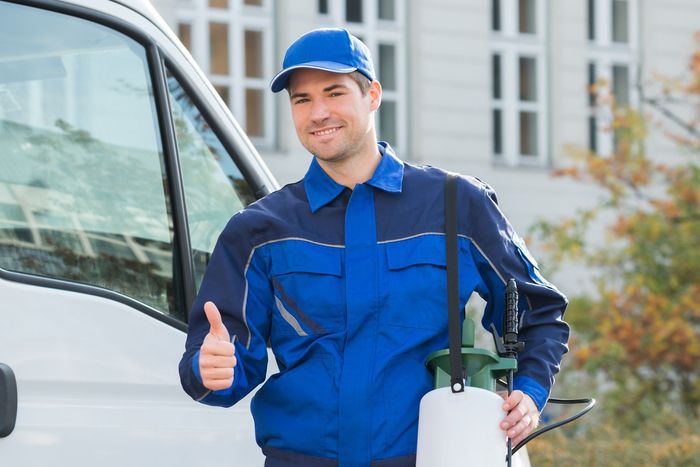 A man is standing in front of a white van holding a sprayer and giving a thumbs up.