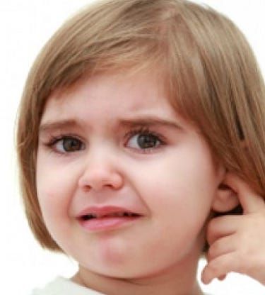 A little girl is holding her ear and making a funny face.