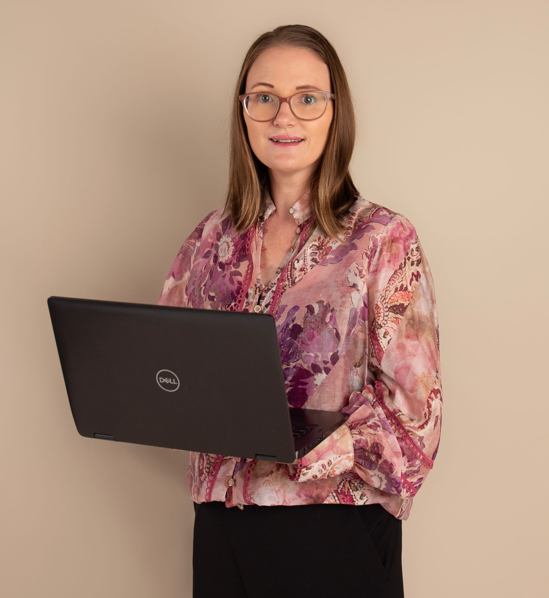 Woman wearing glasses and floral shirt, holding an open laptop.