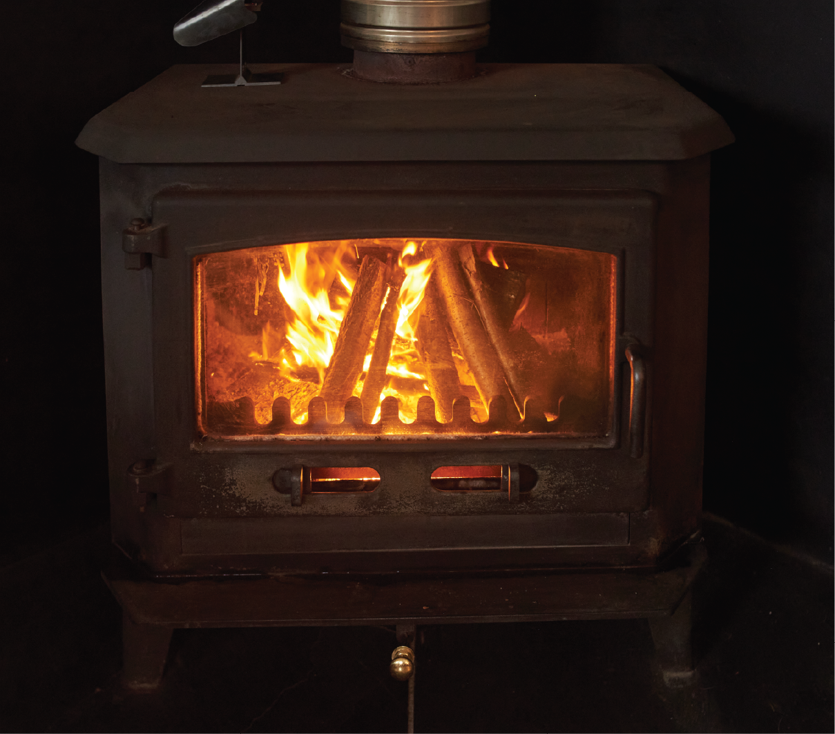 A wood stove is lit up in a dark room.