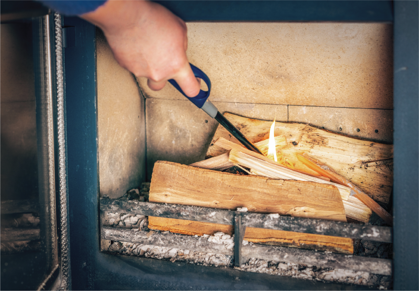 A person is lighting a fire in a fireplace with a lighter.