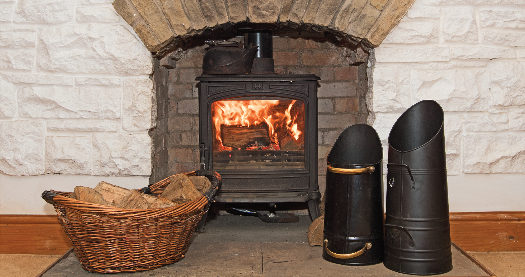 A wood stove is sitting in a fireplace next to a basket of logs.