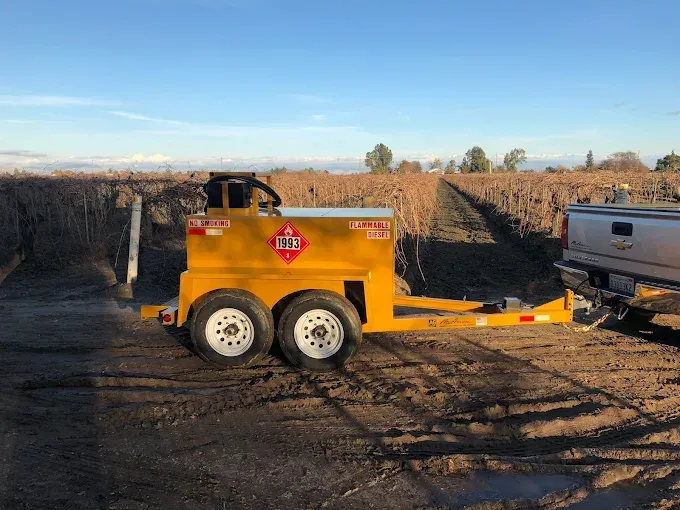 Yellow construction trailer on a dirt lot, hitched to a pickup truck near a trench at sunset.