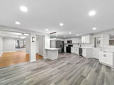 Bright open kitchen and living area with gray flooring, white cabinets, and hardwood dining space.
