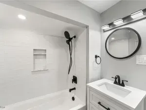 Modern white bathroom with bathtub, black shower fixtures, and round mirror above a white vanity.