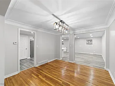 Empty dining room with hardwood floors, gray walls, and a modern chandelier, opening to adjacent rooms.