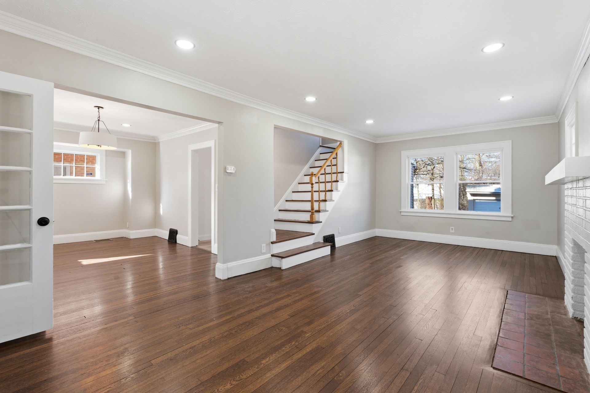 Bright empty living room with hardwood floors, staircase, recessed lights, and windows
