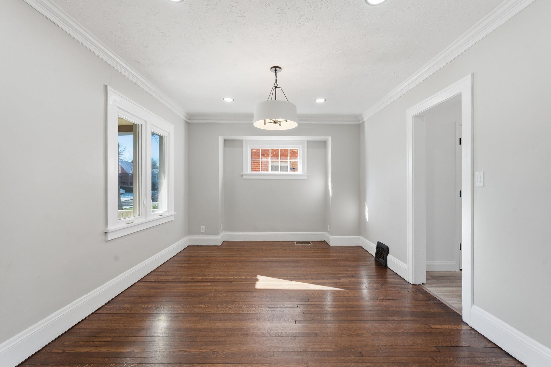 Empty gray room with hardwood floors, white trim, windows, and a ceiling light fixture.