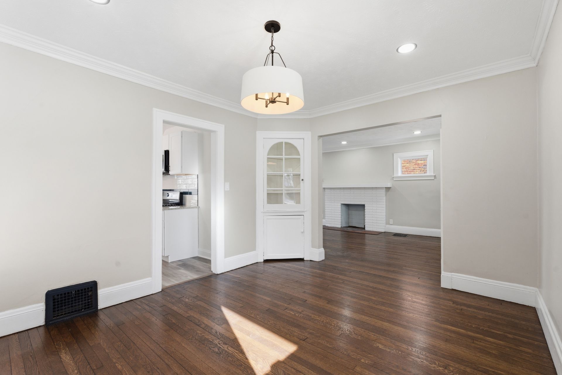 Empty living room with dark hardwood floors, light gray walls, white trim, and a chandelier