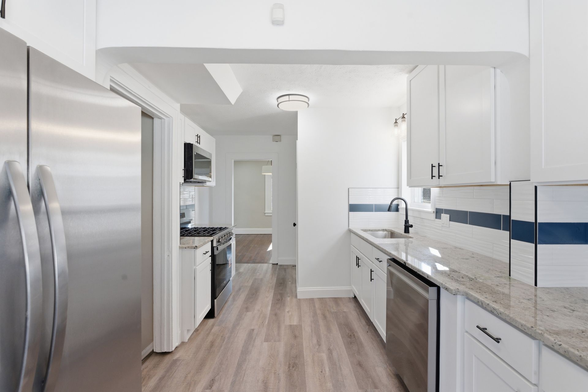 Bright modern kitchen with white cabinets, stainless appliances, blue backsplash, and wood flooring