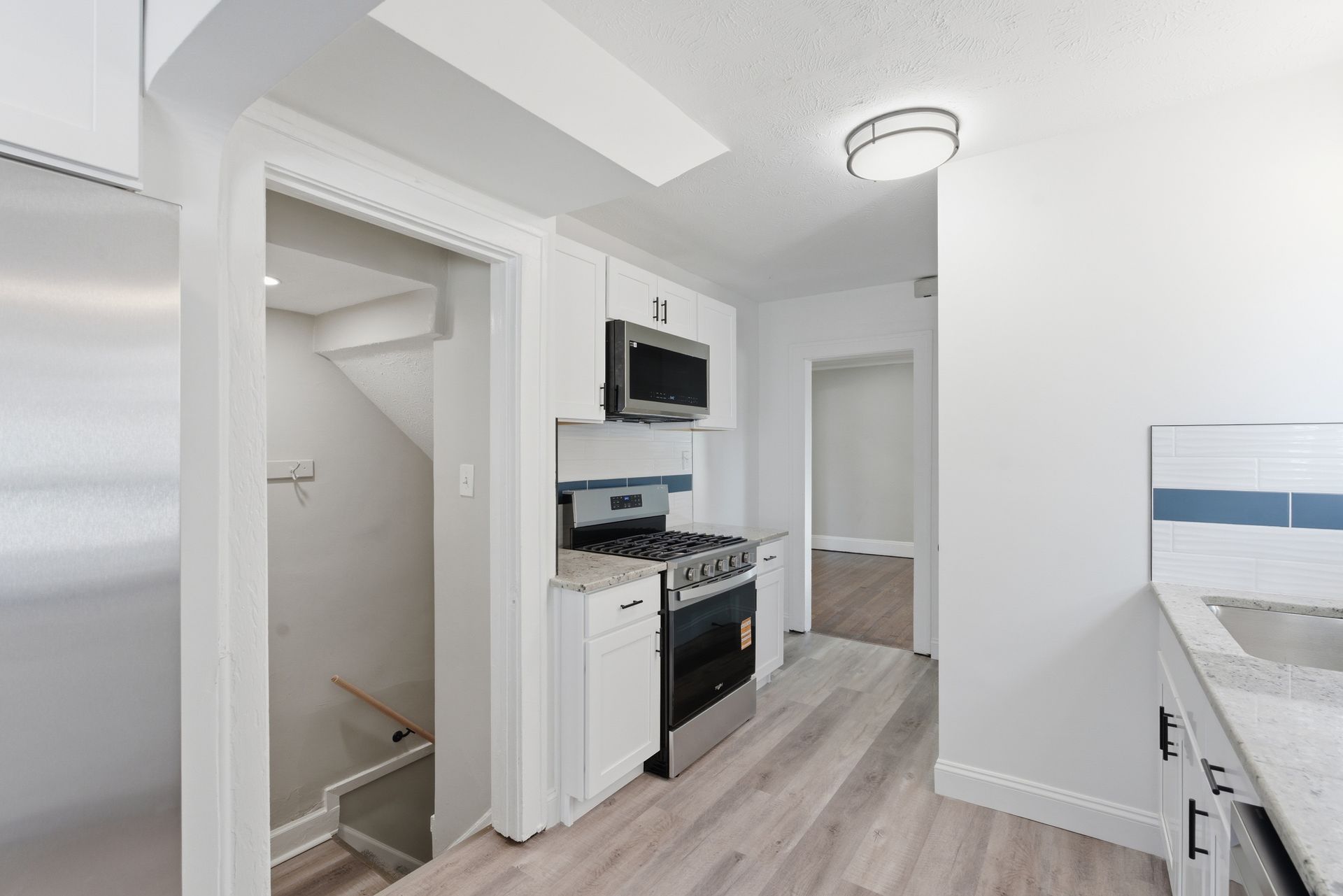 Small white kitchen with stove, microwave, pantry closet, and light wood flooring