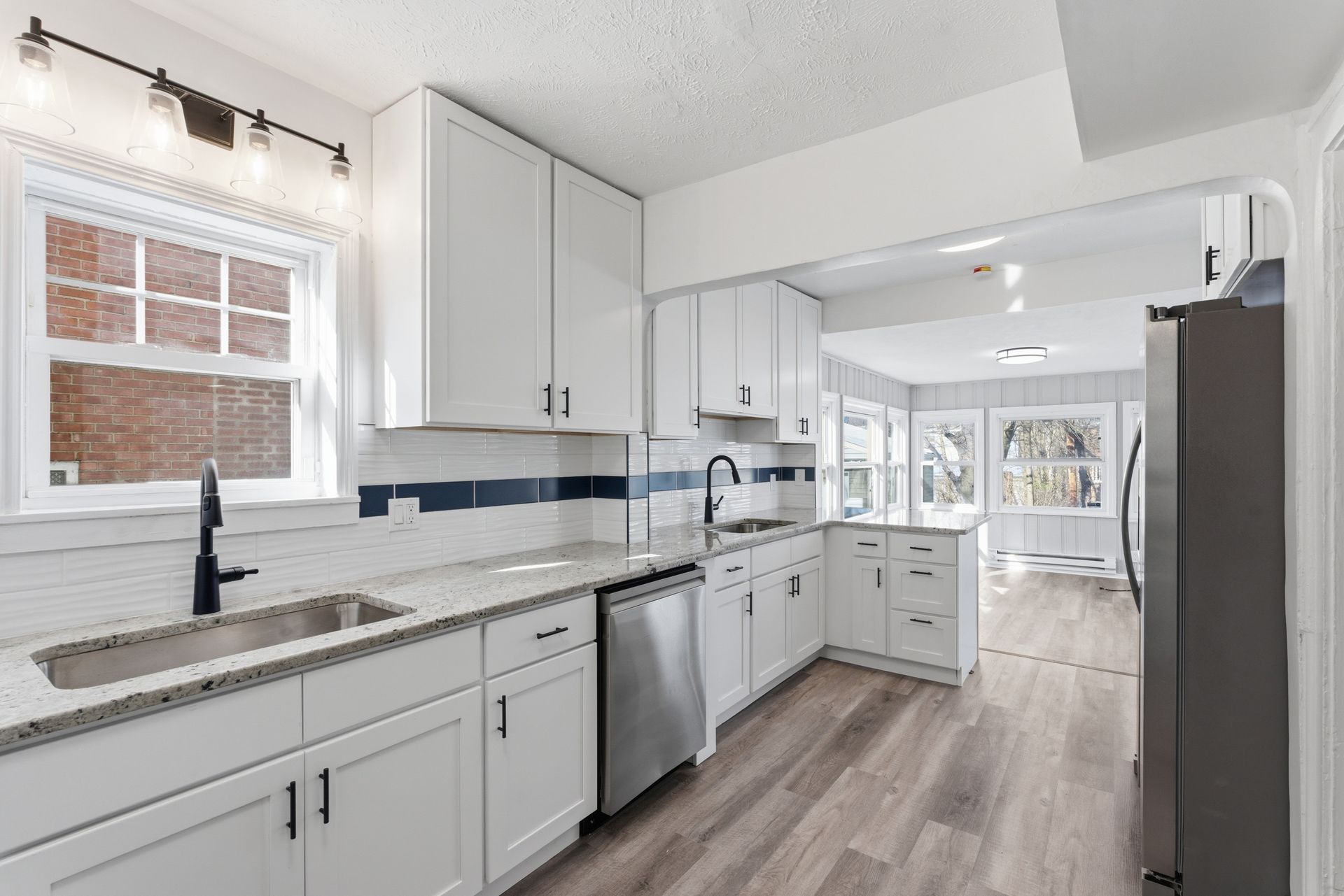 Bright white galley kitchen with quartz counters, stainless appliances, and wood-look floors