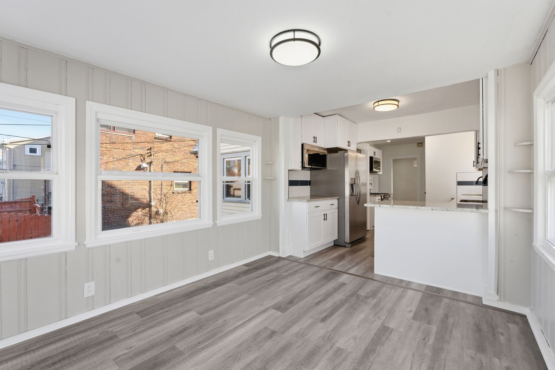 Bright open kitchen with white cabinets, stainless appliances, gray wood floors, and large windows