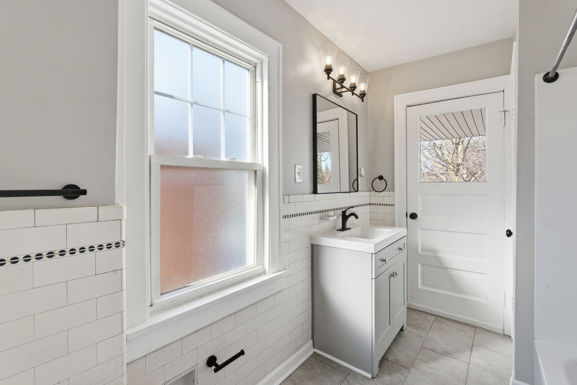 Bright bathroom with white beadboard walls, a vanity sink, window, and frosted glass door.