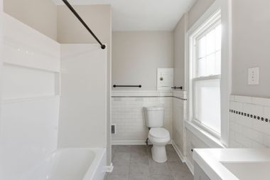 Bright white bathroom with tub, toilet, window, and tiled floor