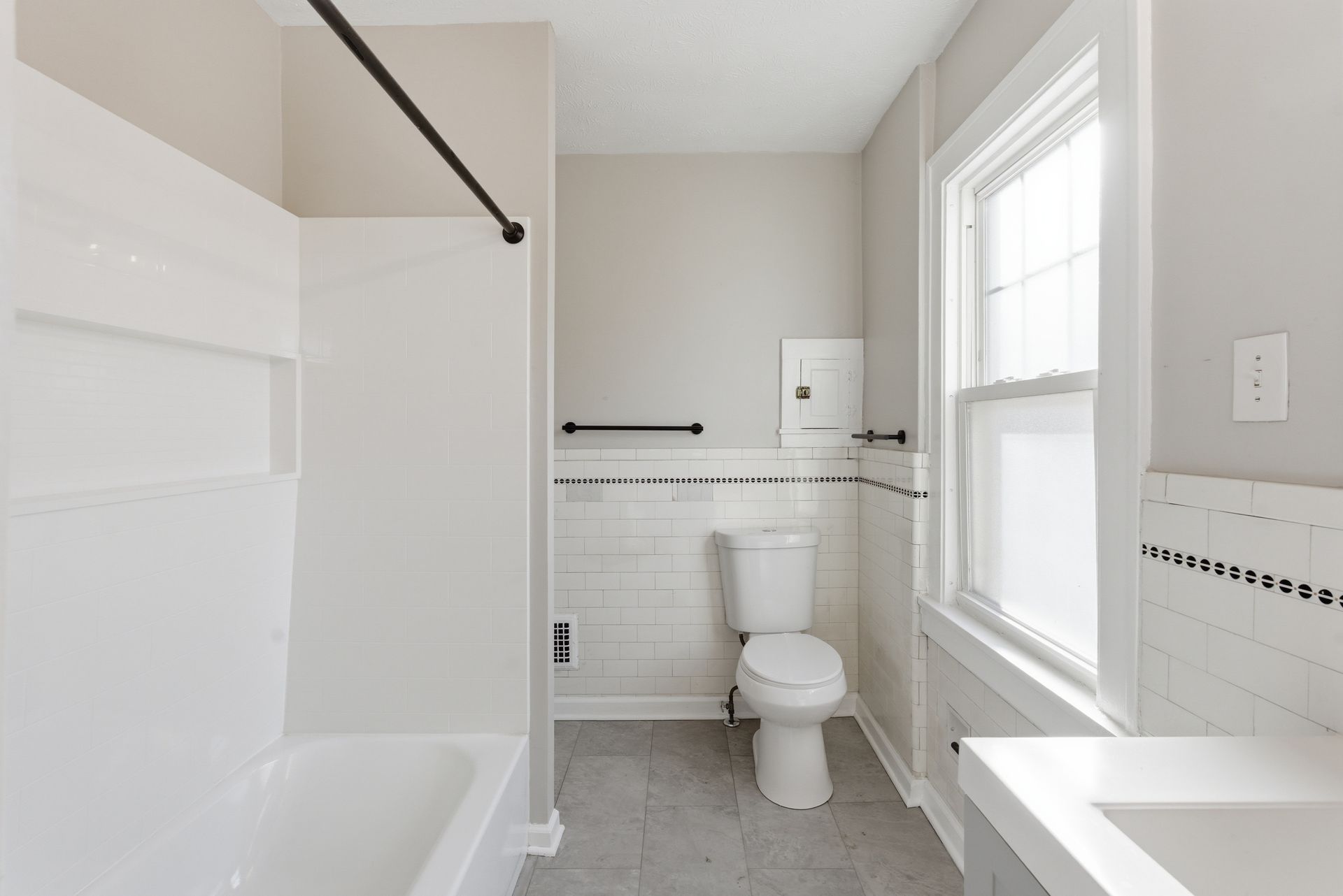 Bright white bathroom with bathtub, toilet, sink, and window.