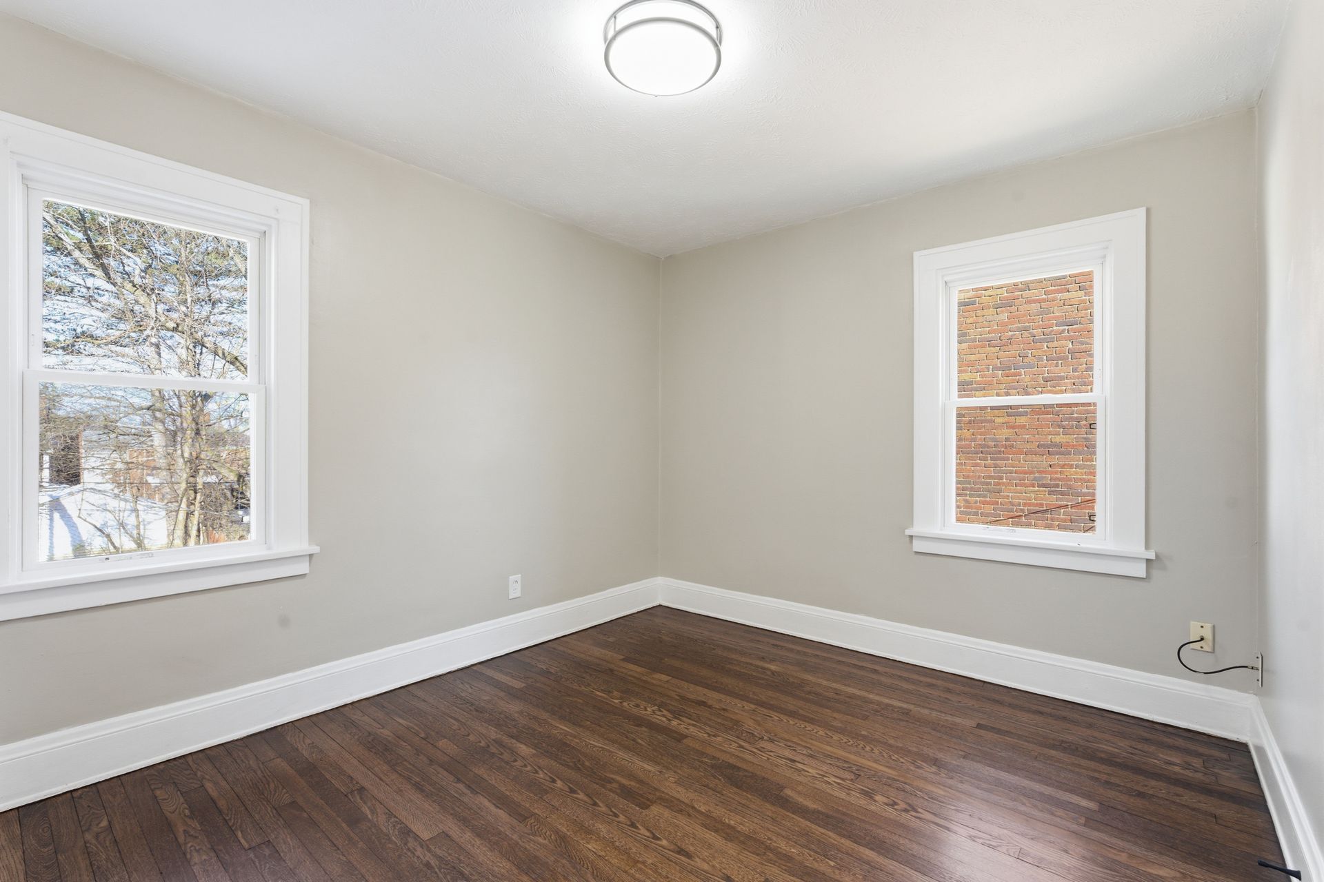Empty room with dark wood floors, light gray walls, two windows, and a ceiling light.