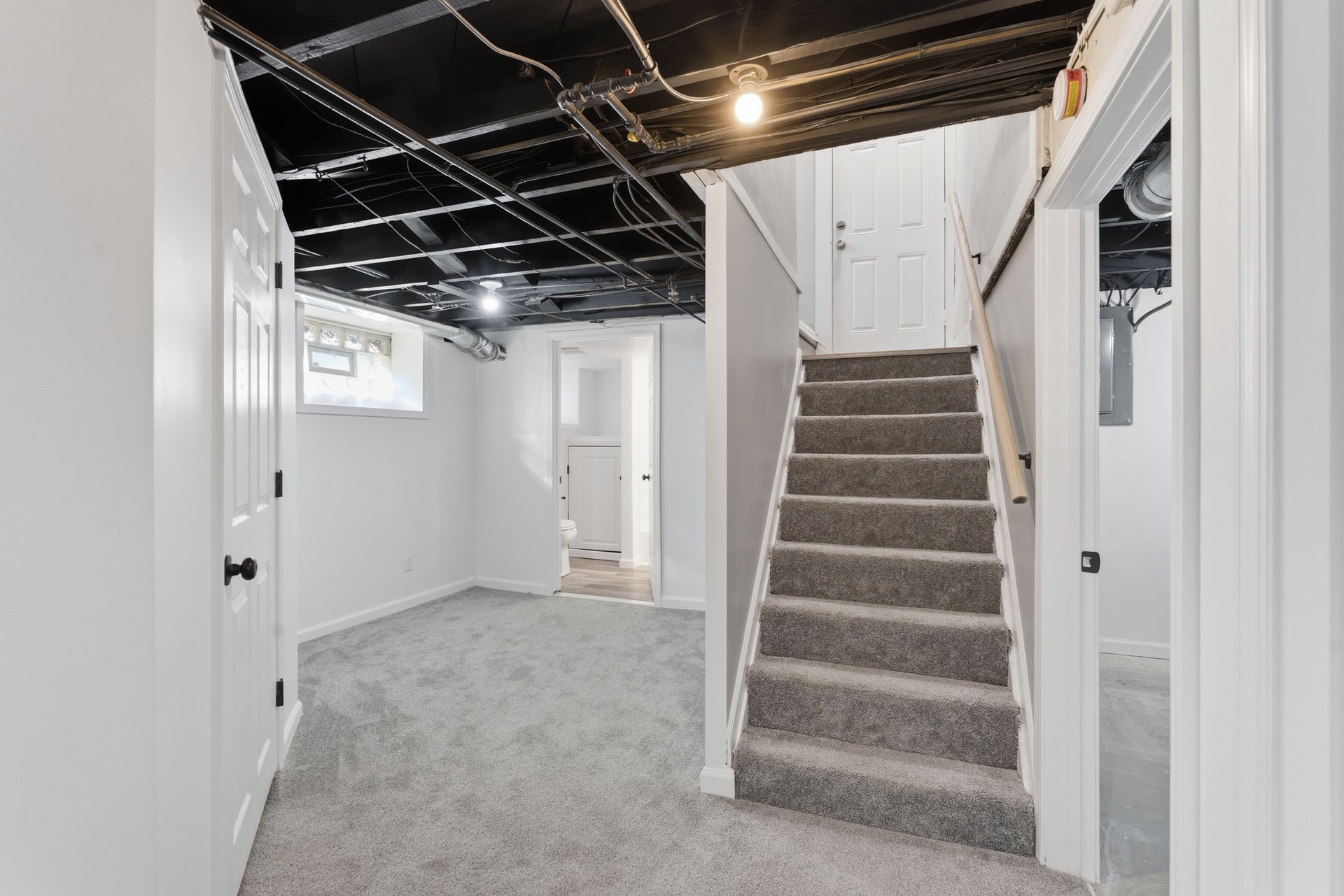Finished basement hallway with carpeted stairs, white walls, and exposed ceiling joists