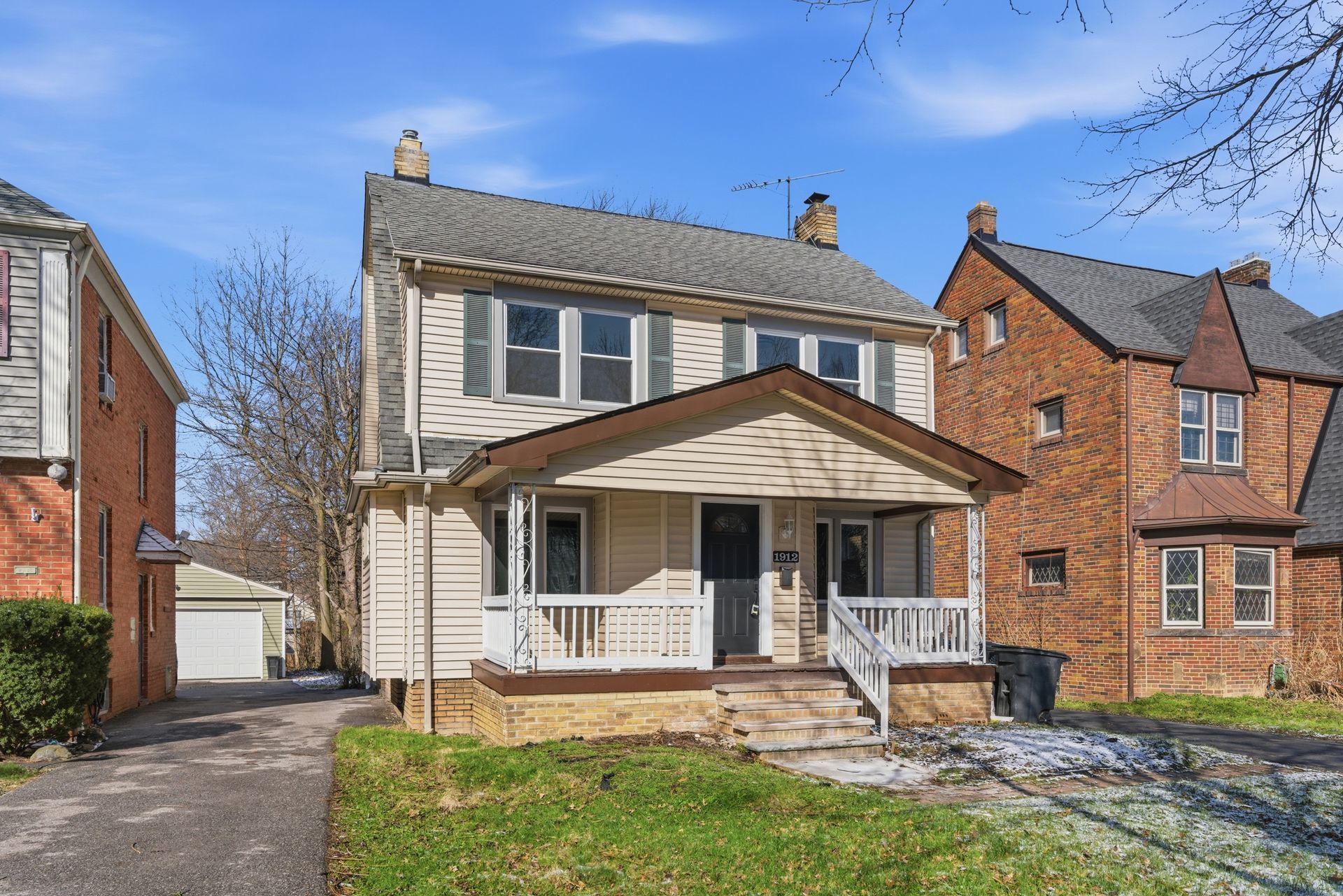 Two-story white house with front porch and driveway on a sunny suburban street