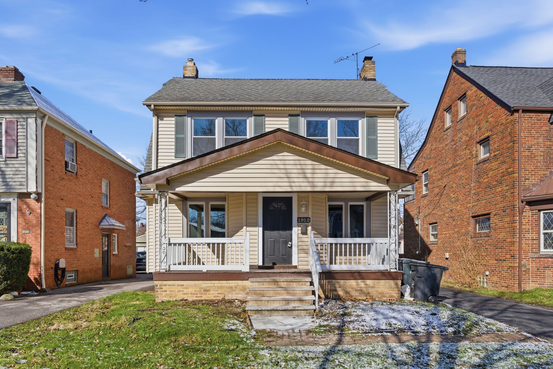 Two-story brick house with a white front porch and steps, viewed from the front under a blue sky