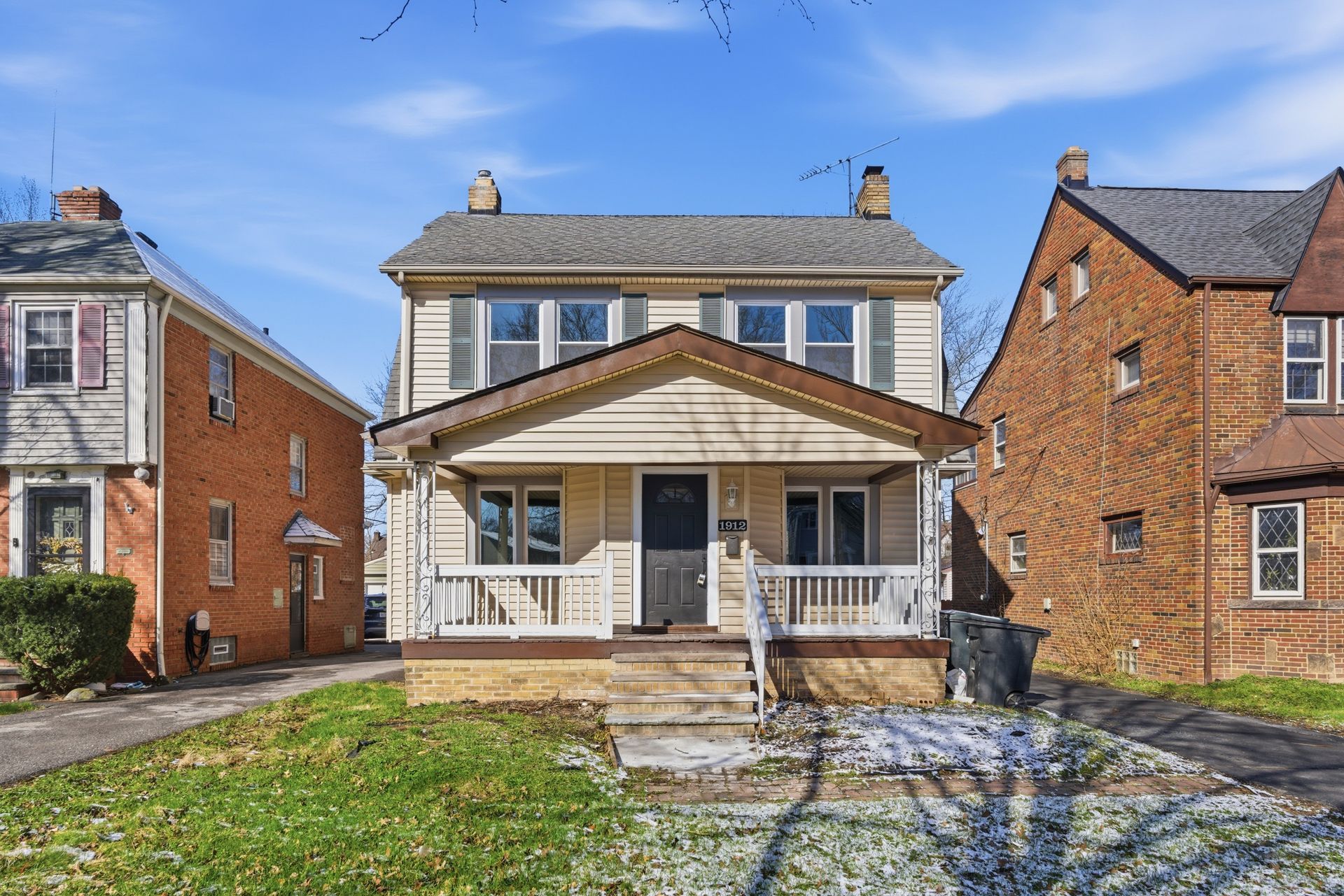 Front view of a two-story brick house with a covered porch and concrete driveway under a blue sky
