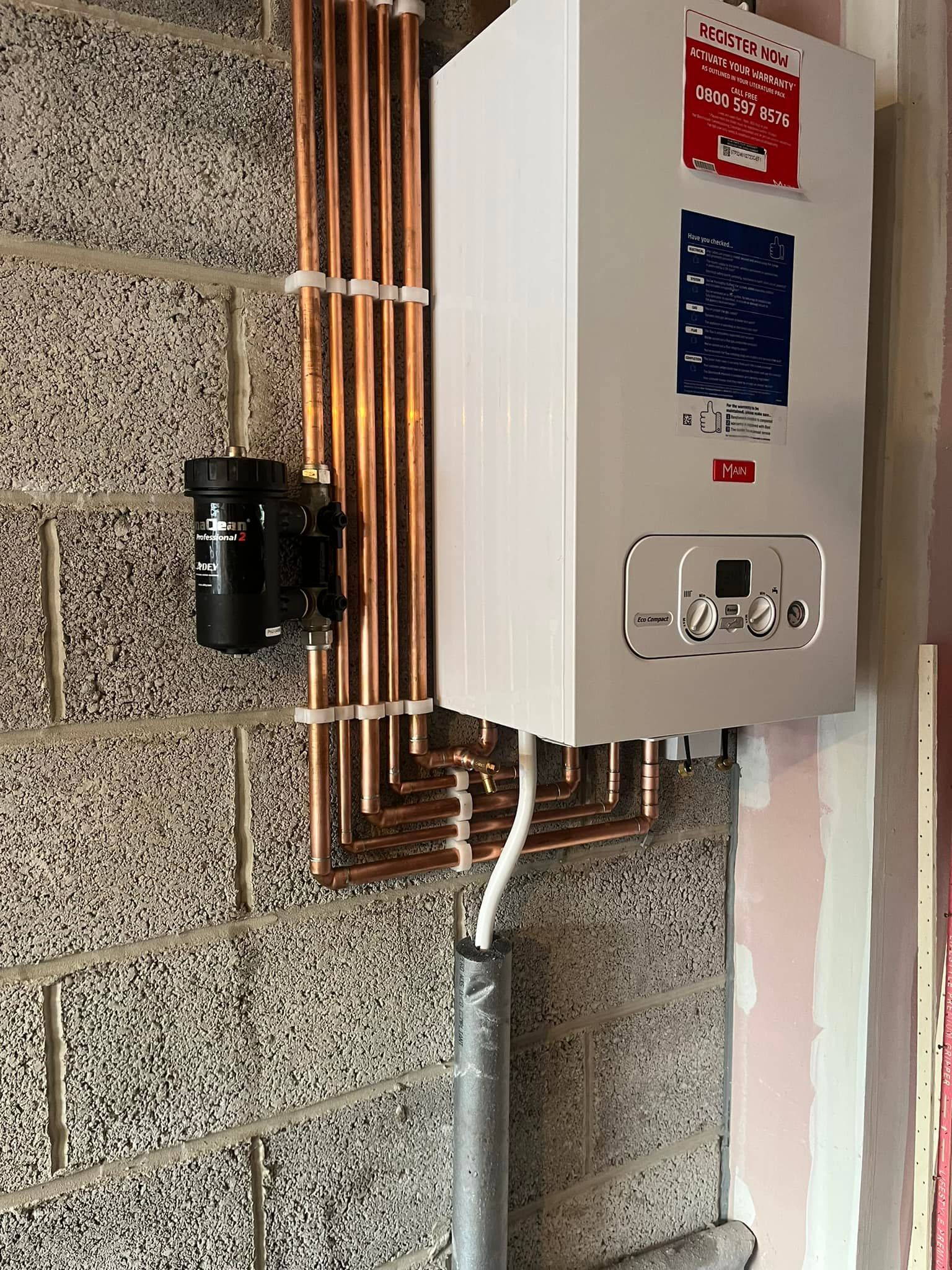 White boiler unit and copper pipes installed on a gray brick wall with a black filter.