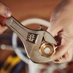 Hands using a wrench to tighten a brass fitting.