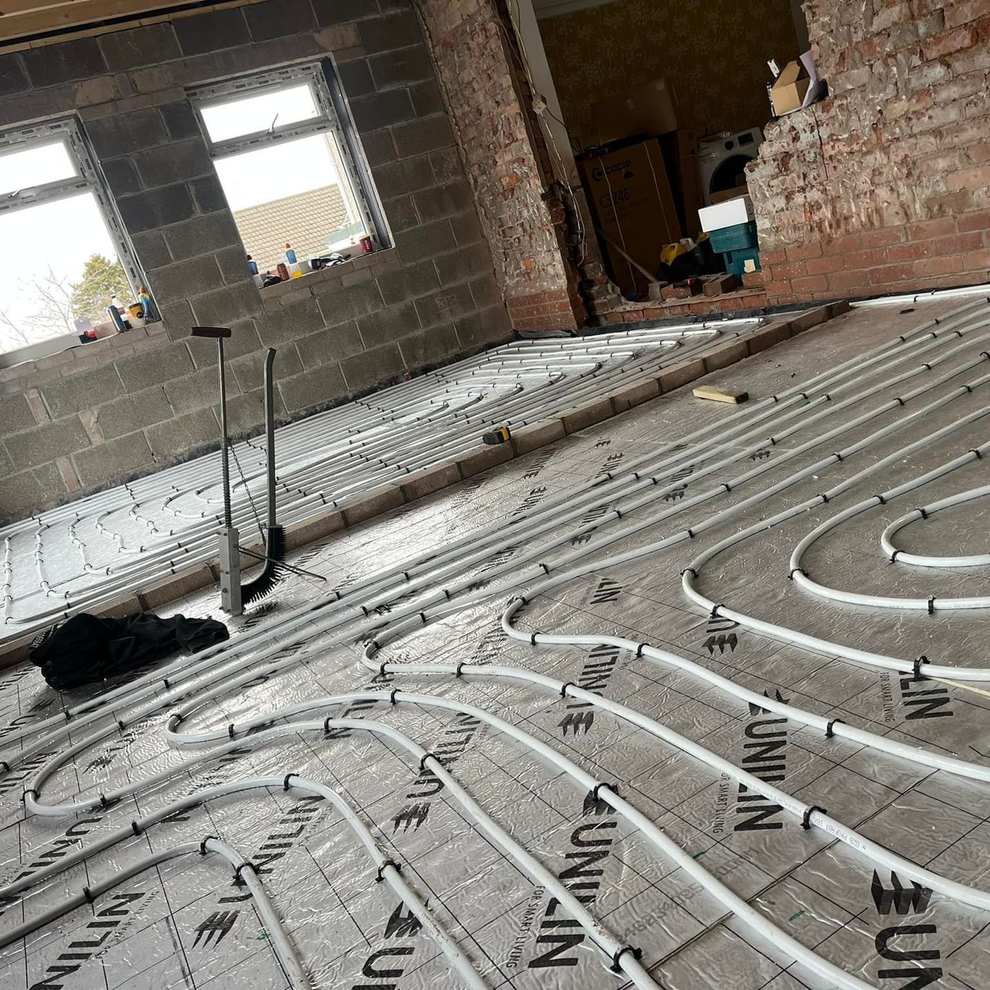 Underfloor heating installation in a room with exposed brick and concrete block walls.