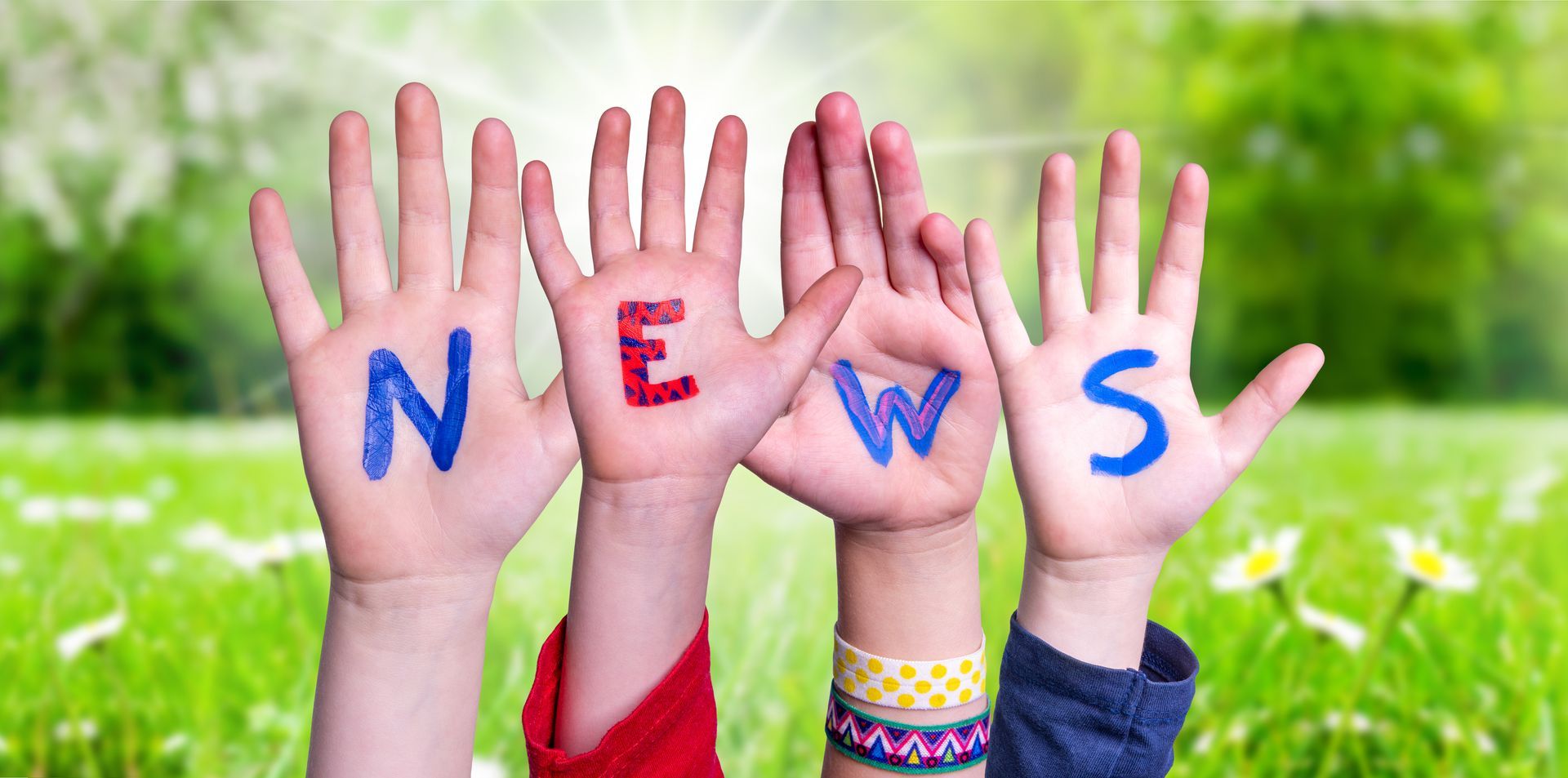 A group of children are holding up their hands with the word news painted on them.