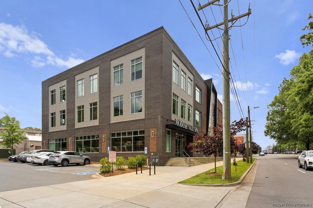 A large Midwood Charlotte building with a lot of windows is sitting on the corner of a street.