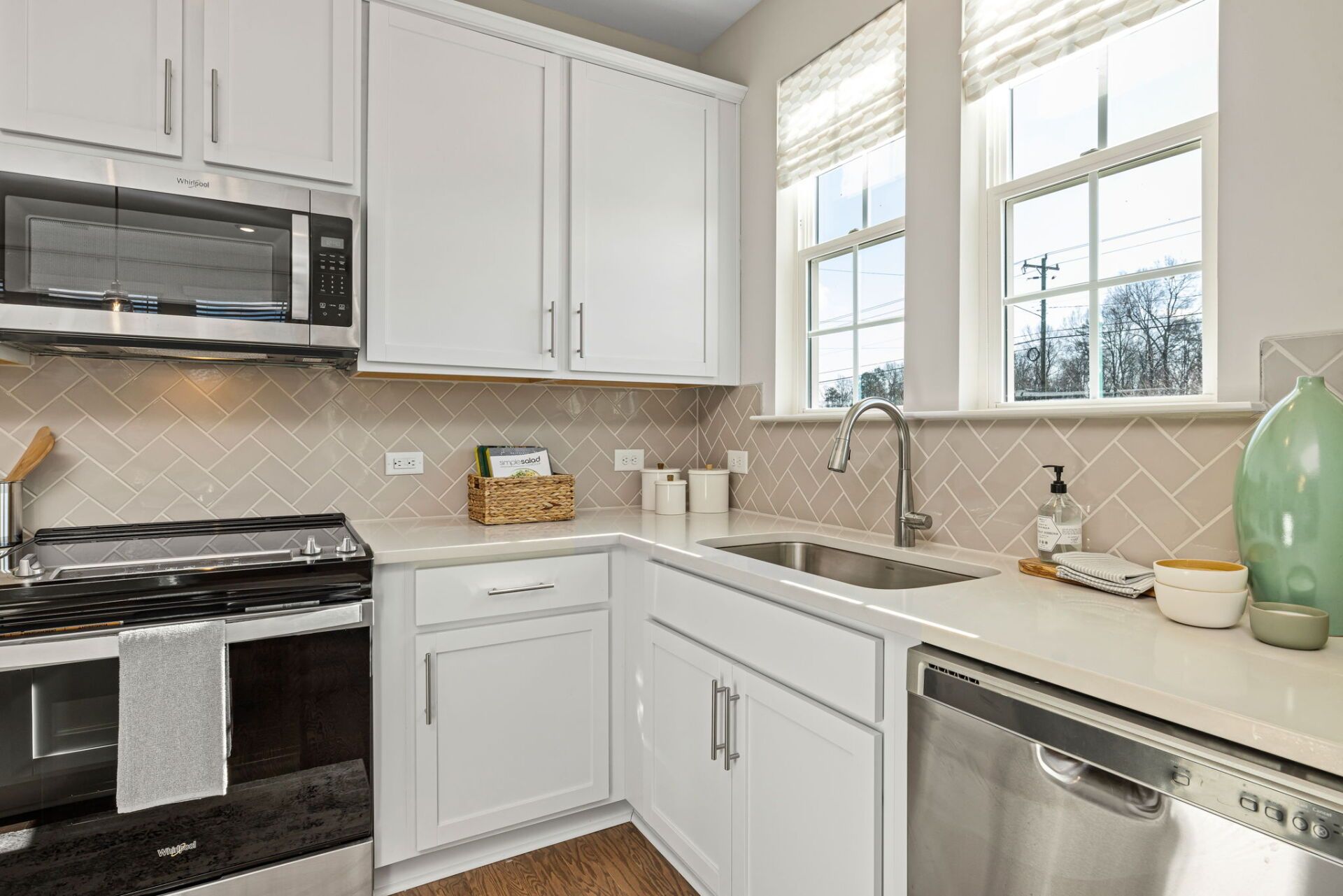 White kitchen with stainless steel appliances, cabinets, and a window over the sink.