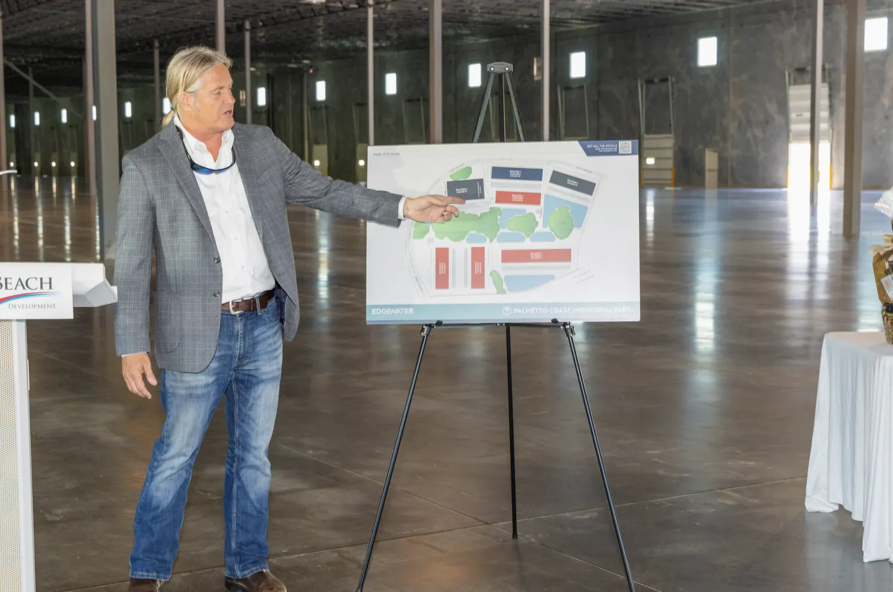 A man in a suit is standing in front of an easel holding a map.