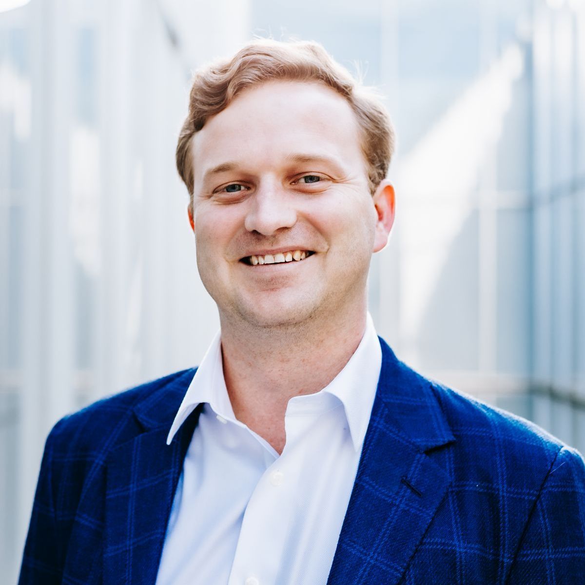 A man in a blue suit and white shirt smiles for the camera