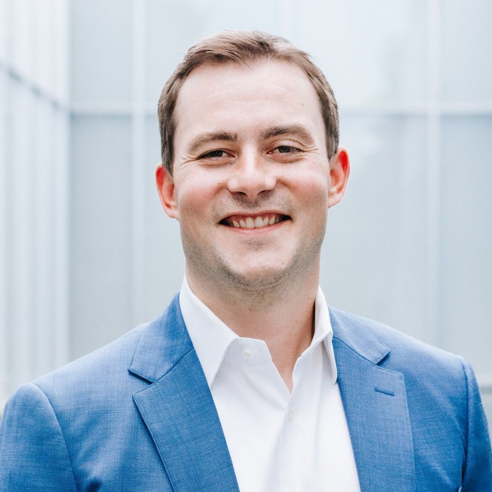 A man in a blue suit and white shirt is smiling for the camera.
