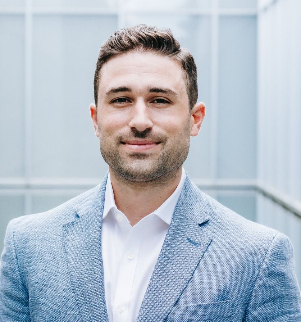 A man in a blue suit and white shirt is smiling for the camera.