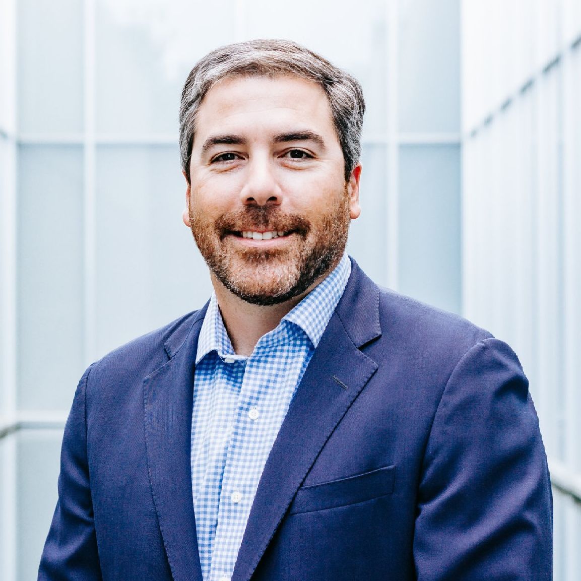 A man in a suit and plaid shirt is smiling for the camera.