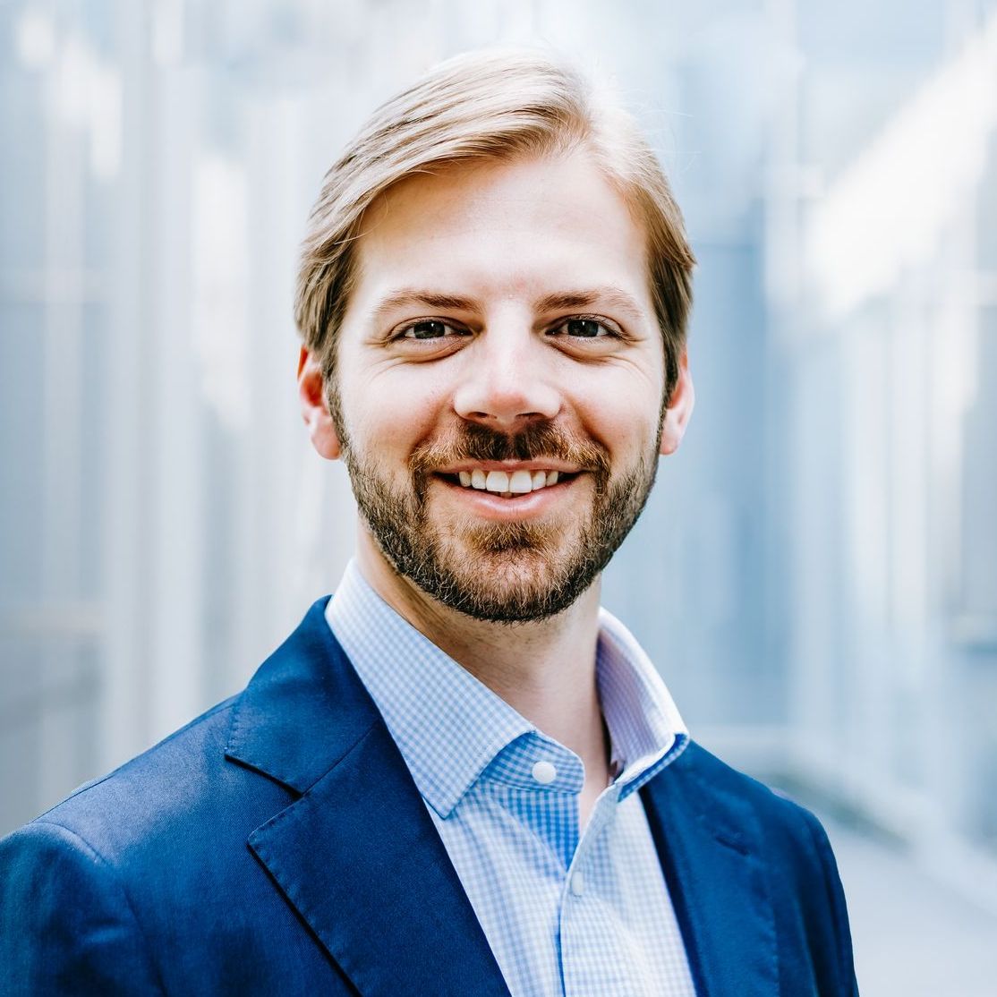 A man with a beard is wearing a blue suit and smiling for the camera.
