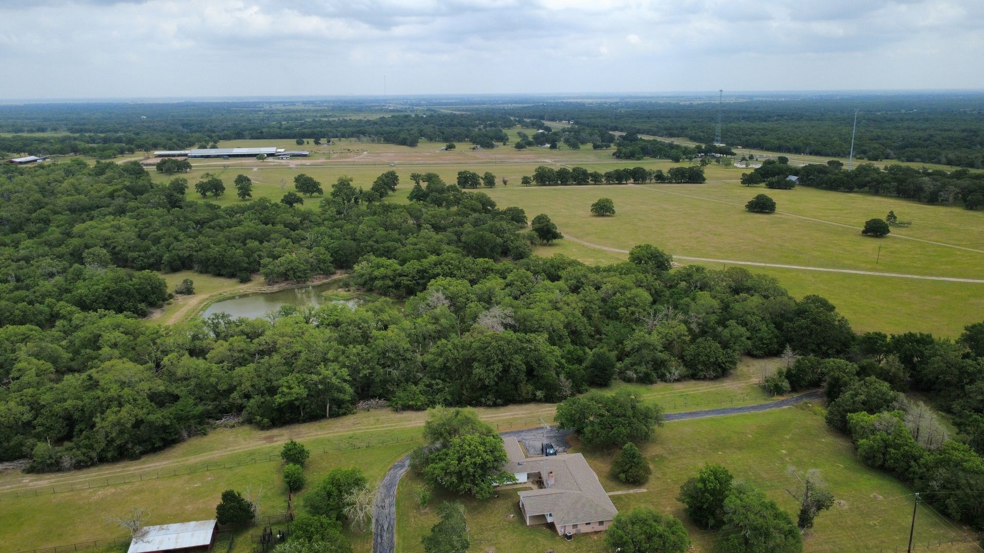 An aerial view of a house in the middle of a field surrounded by trees.