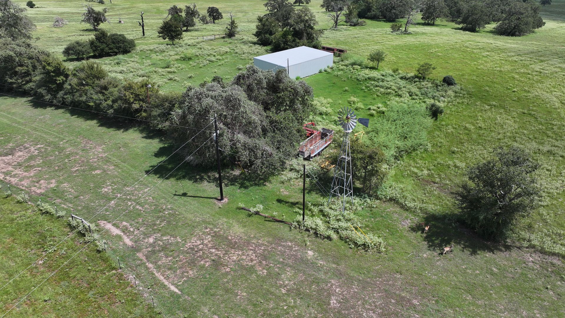 An aerial view of a house in the middle of a grassy field surrounded by trees.
