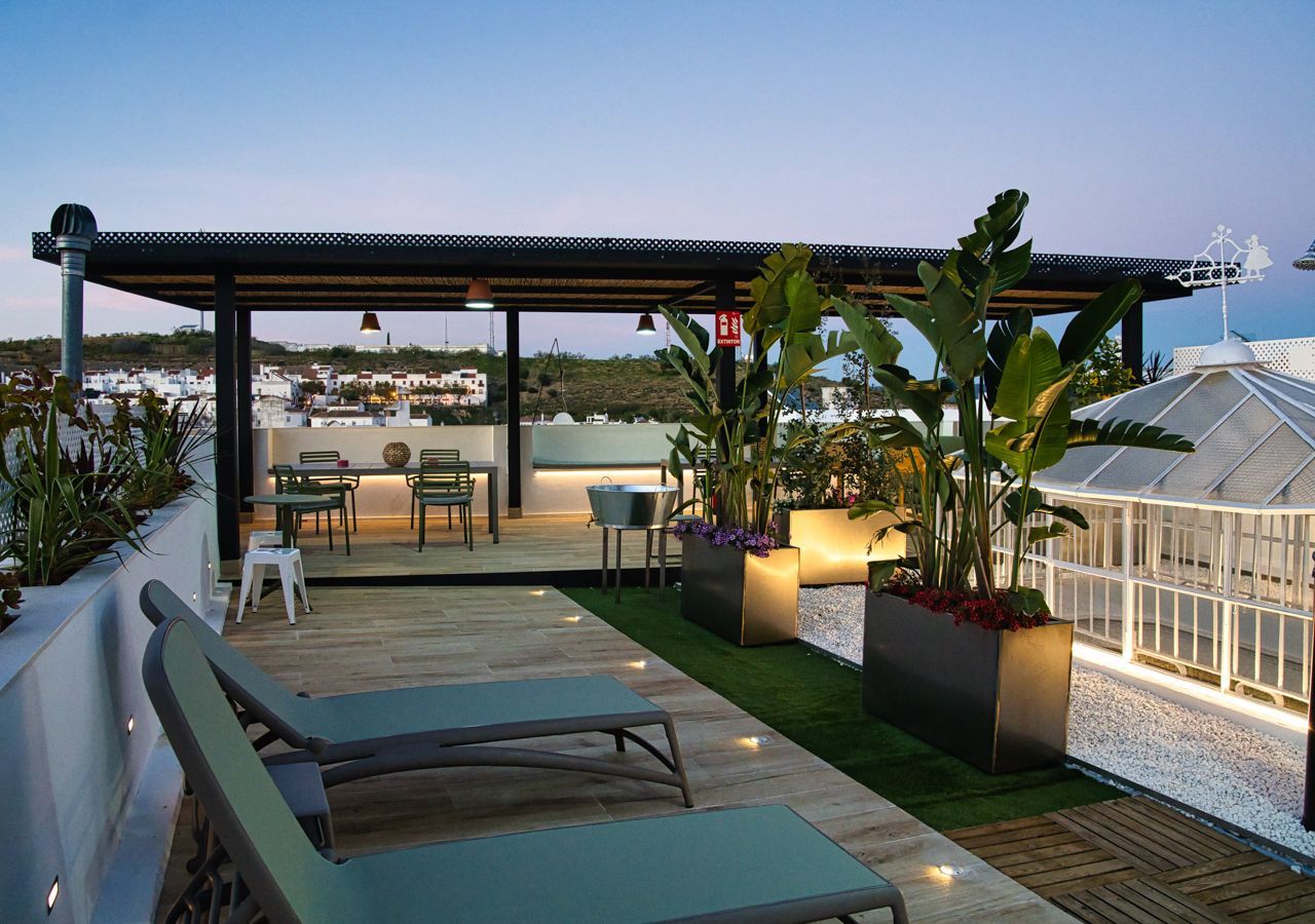 Patio en la azotea con tumbonas, zona de comedor y plantas en macetas, bañado por la luz del atardecer.
