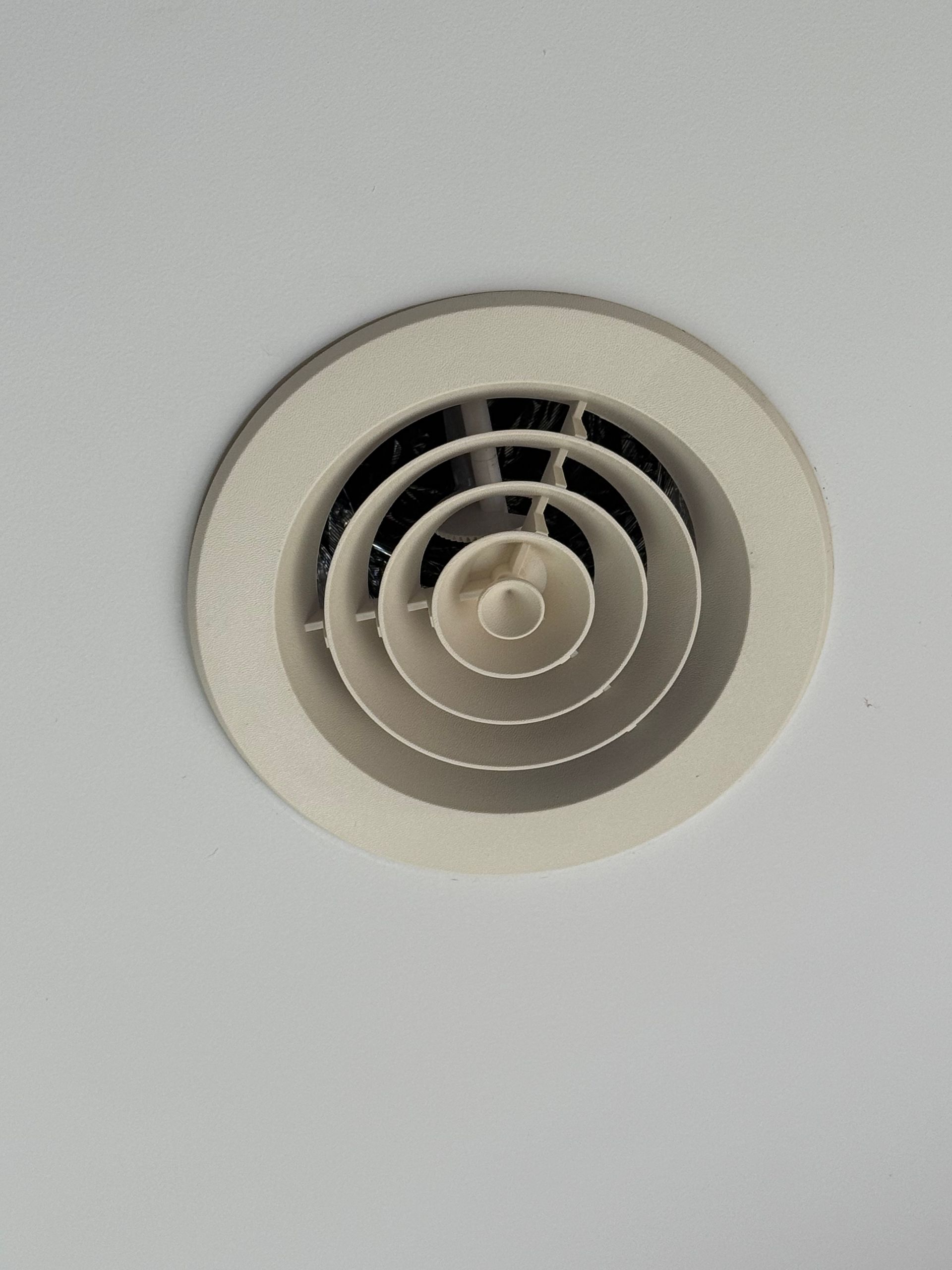 A white, circular HVAC ceiling diffuser with concentric rings mounted on a white ceiling. — Priest Airconditioning in Ashmont, NSW