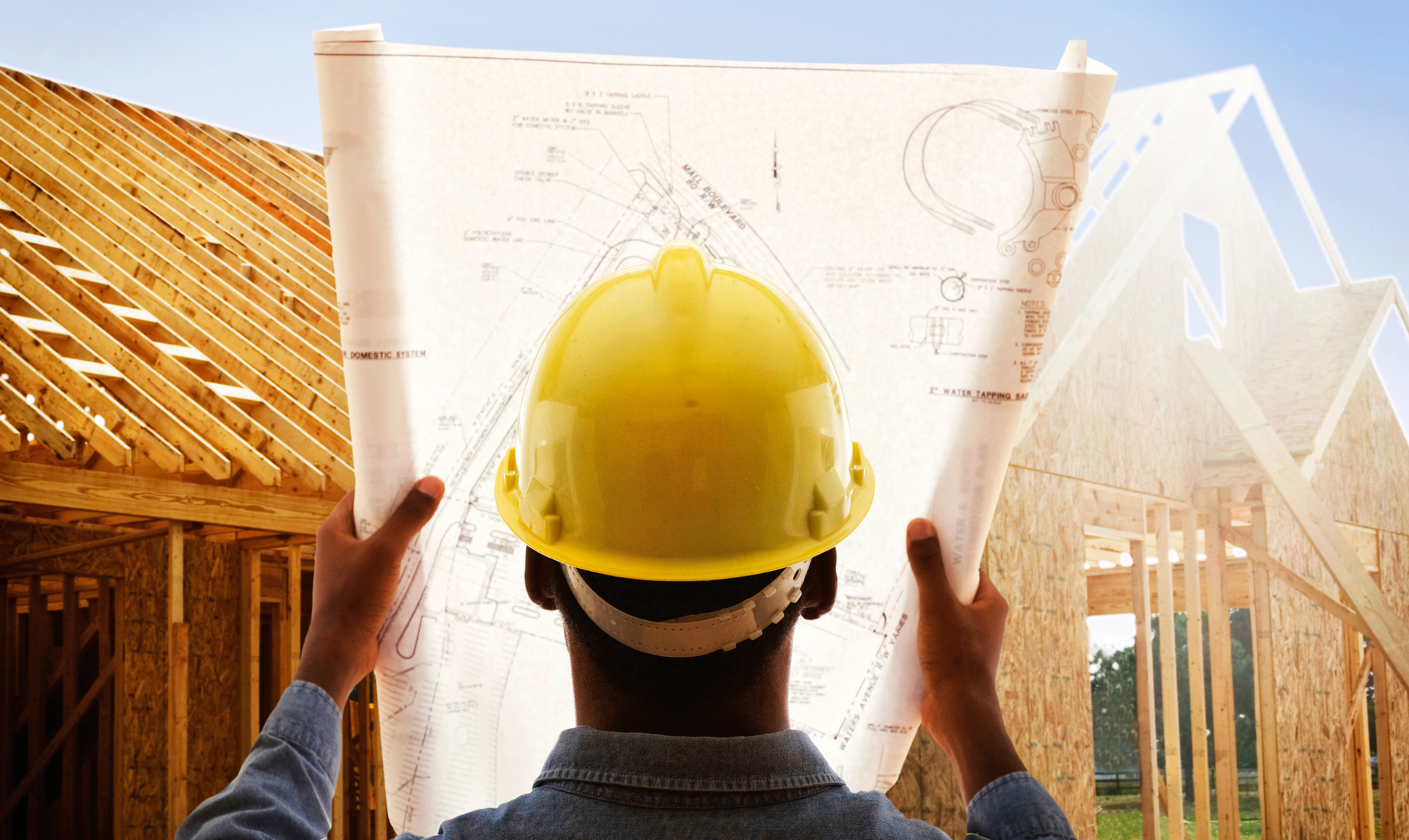 Construction worker in yellow hard hat reviewing blueprints at a construction site.