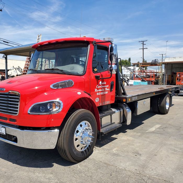 A red flatbed tow truck is parked in a parking lot.