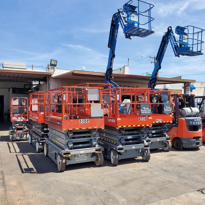 A row of scissor lifts are parked in front of a building