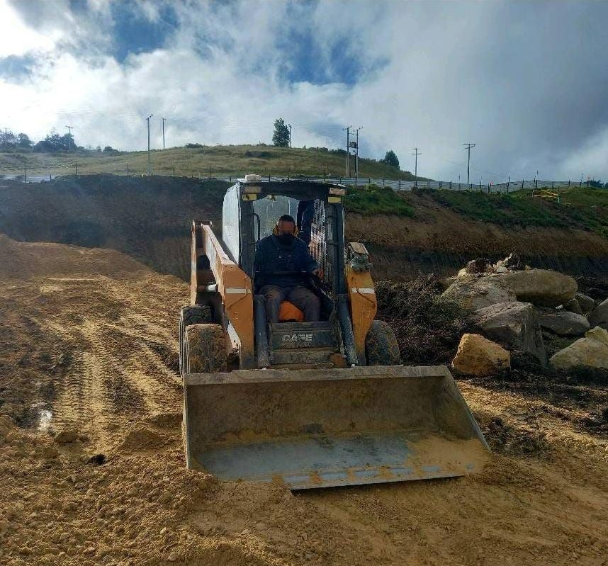 Un hombre conduce una excavadora por un camino de tierra.