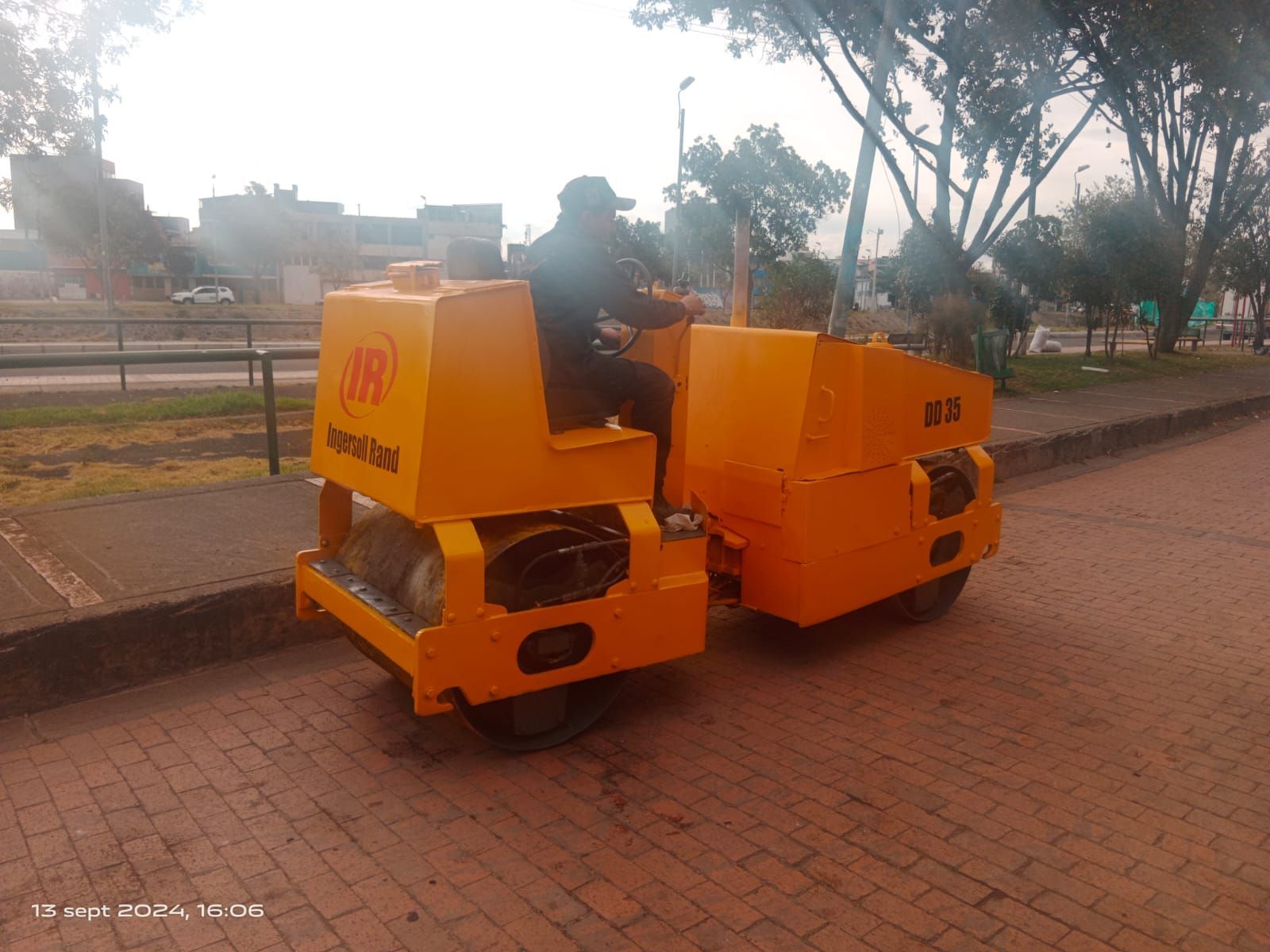 Un hombre conduce un rodillo amarillo sobre una acera de ladrillos.