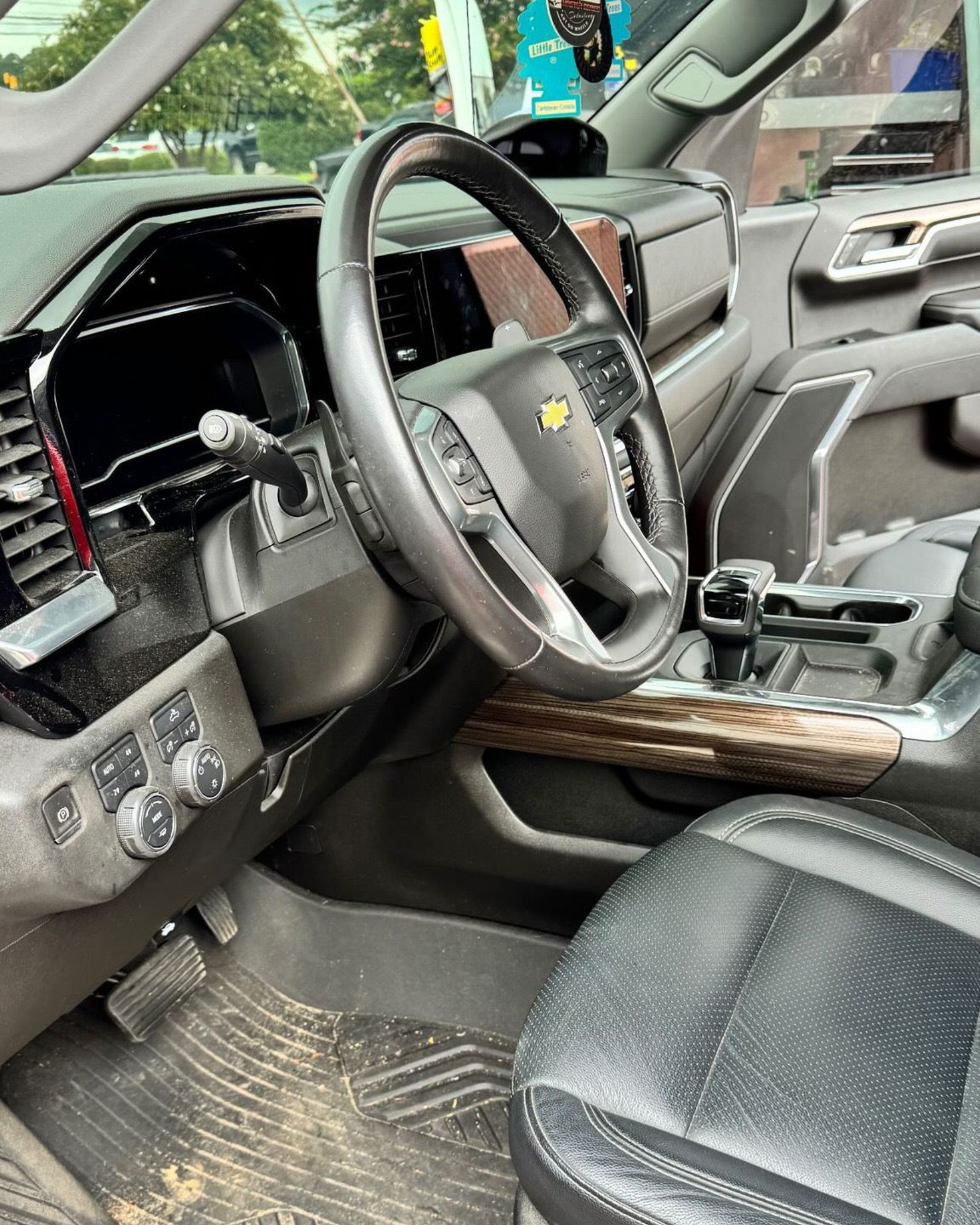 Interior view of a black Chevrolet truck's driver seat, dashboard, and steering wheel; wood trim accents.