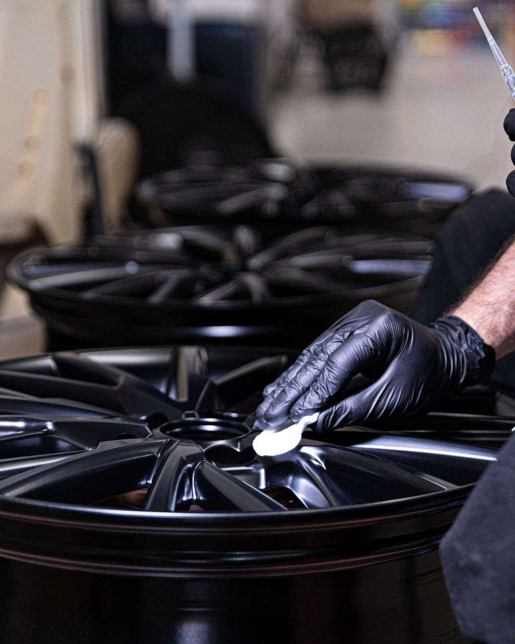 Person in black gloves cleaning a black car wheel in a workshop.